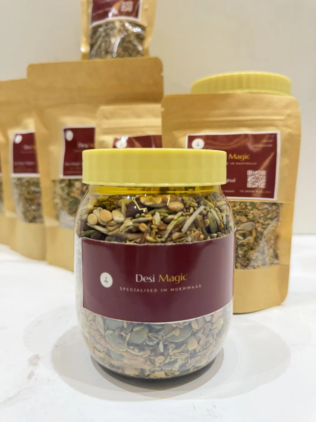 A Desi Magic jar of mukhwaas with a yellow lid, in front of kraft pouches